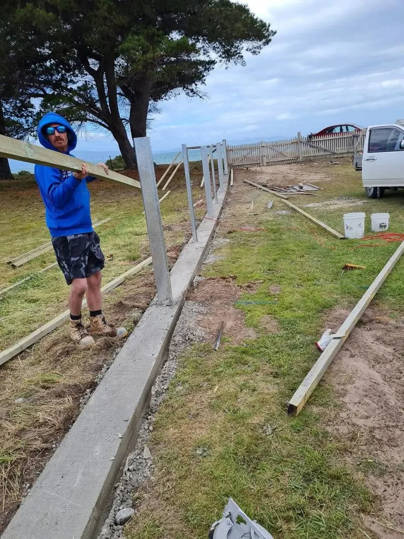 Carrying a timber rail along a new fence line with steel posts set in concrete