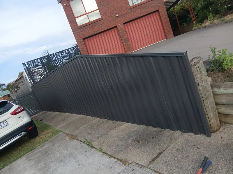 Dark Colorbond fence running along a driveway beside a brick garage
