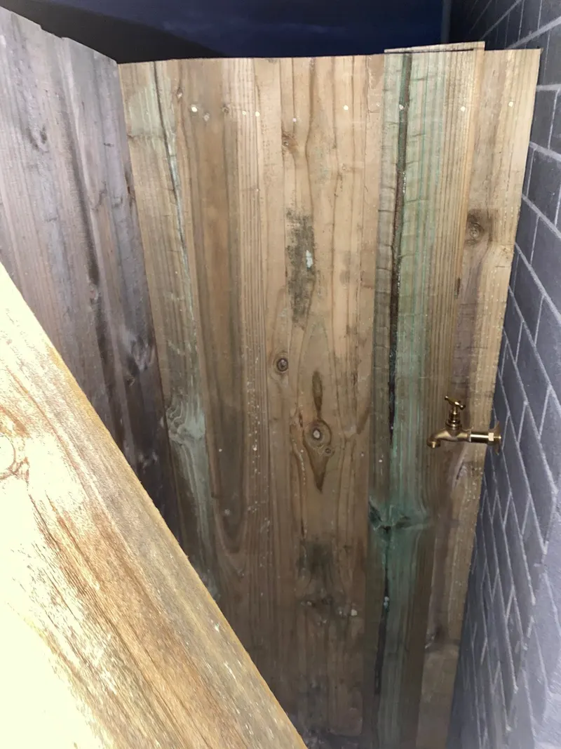 A timber paling gate with a brass latch beside a brick house